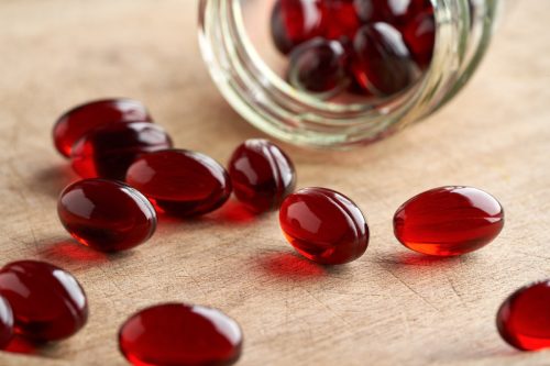 Krill oil pills poured from a glass jar onto the table