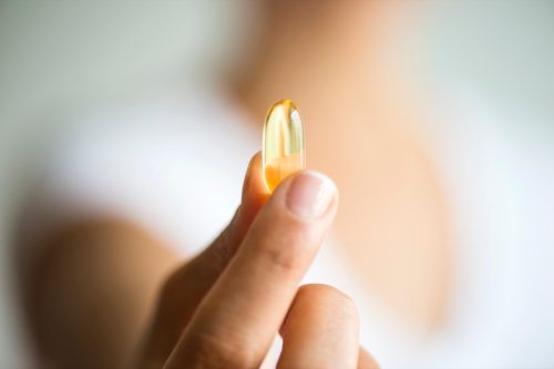 A woman is holding an omega-3 capsule.